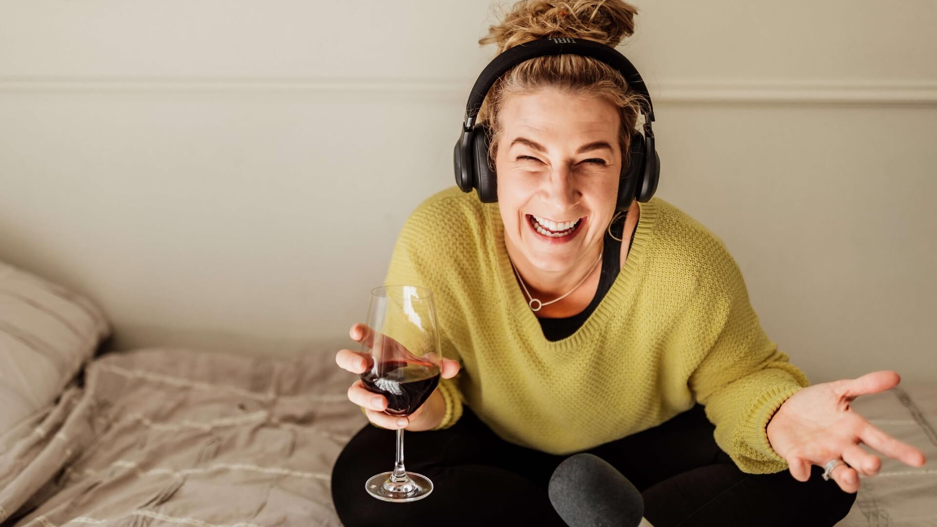 Lou Fitz laughing on a bed in headphones, holding a drink, recording the Getting Vulnerable podcast